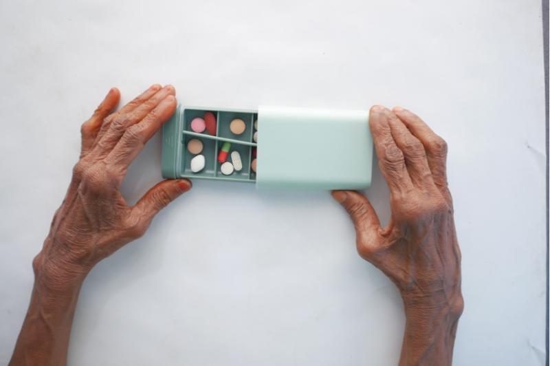 A top-down view of an elderly person’s hands while holding a medicine box on a table.