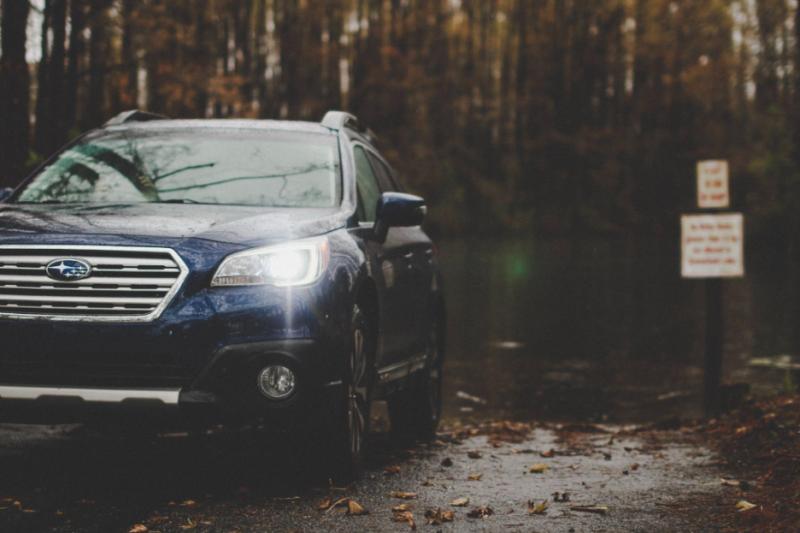 A Subaru sits in a wet forested parking lot, representing the kinds of cars that CarGuard protects