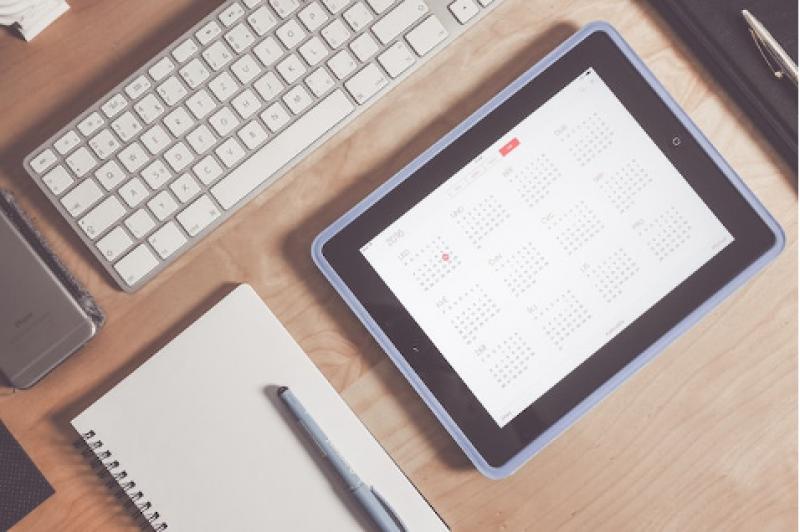 A calendar on a tablet next to a keyboard and a notebook